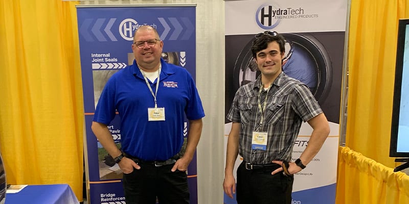 Peter and Caleb Standing In Front Of The HydraTech Booth At OTEC