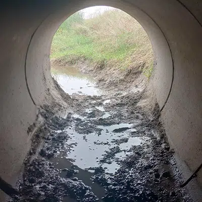 Looking out of a pipe with mud covering the invert