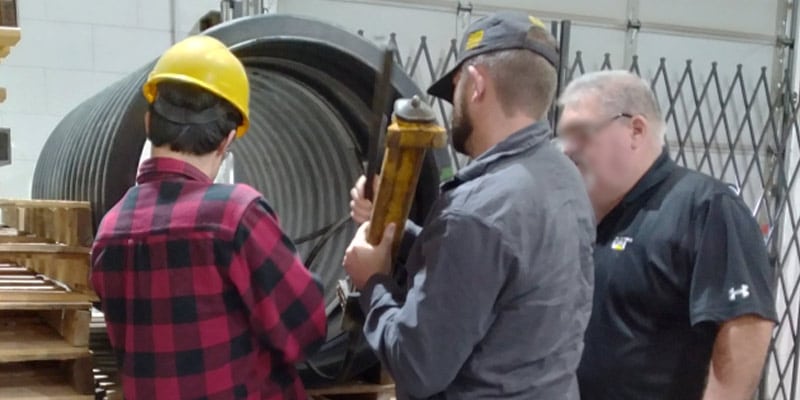 Three people looking at a piece of pipe in which they are installing HydraTite