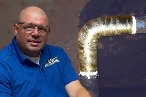 A guy sitting in front of a elbow pipe wrapped in carbon fiber wrap