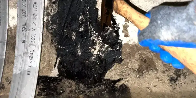 A hammer being used to scrap away a failing repair over a pipe joint