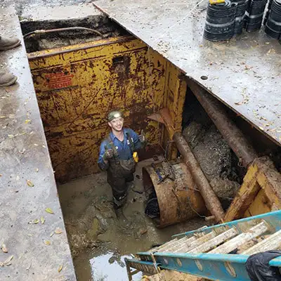 A technician at the bottom of a ladder near a pipe entry point