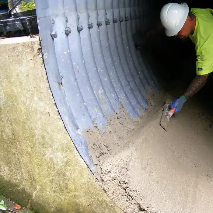 A field crew member smoothing out concrete over an invert of a culvert