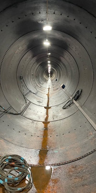 A long penstock pipe with lights running along the crown of the pipe