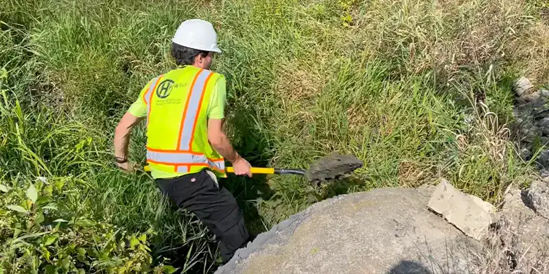 A field technician digging out mud from a stormwater culvert
