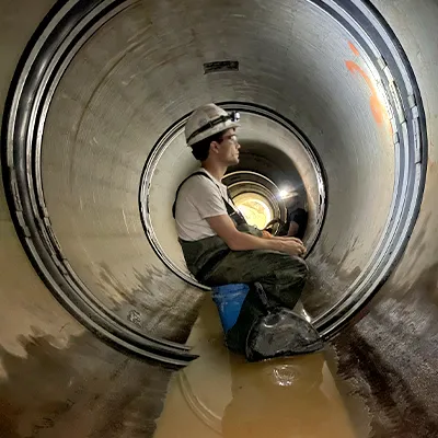 A technician sitting in a pipe, installing HydraTite over a joint