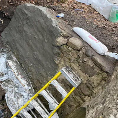 Concrete being applied to an aging headwall with technicians using ladders