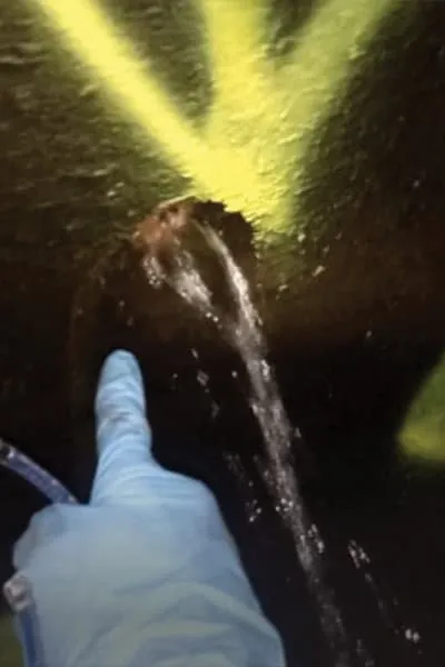 A gloved hand pointing to a leak in a pipe