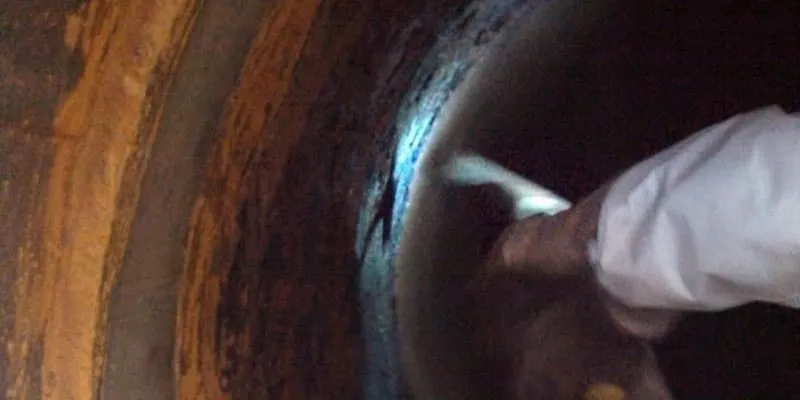 A hammer being used to remove build-up near a joint inside a 30" pump suction line