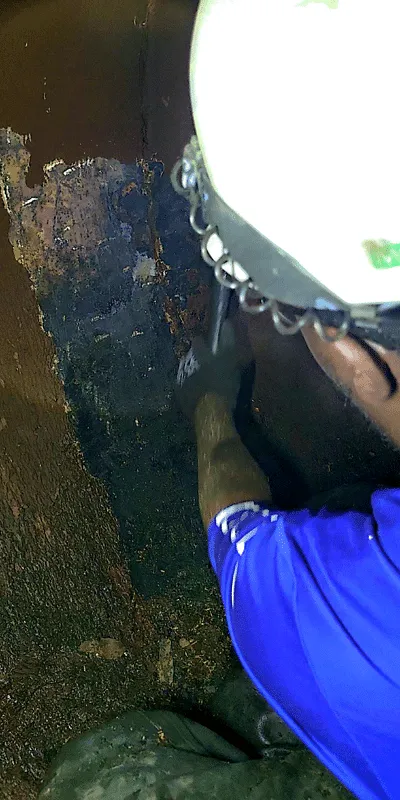 A technician using a hammer to remove tuberculation from the interior wall of a pipe near a joint