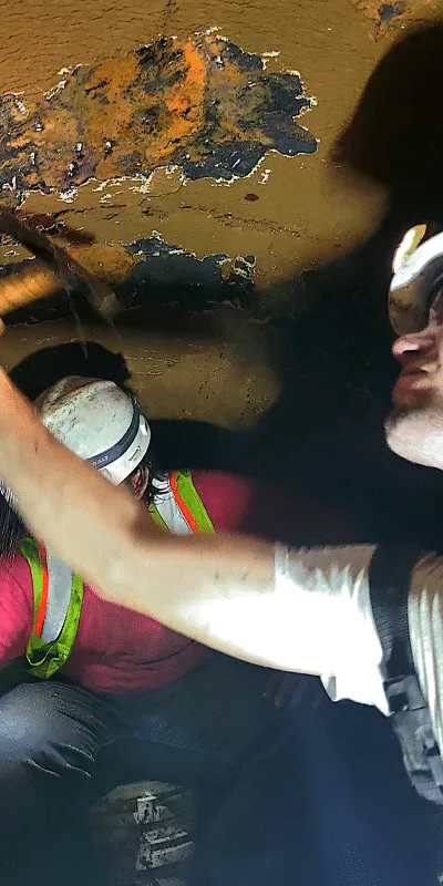 A technician using a hammer to remove tuberculation from the interior wall of a pipe