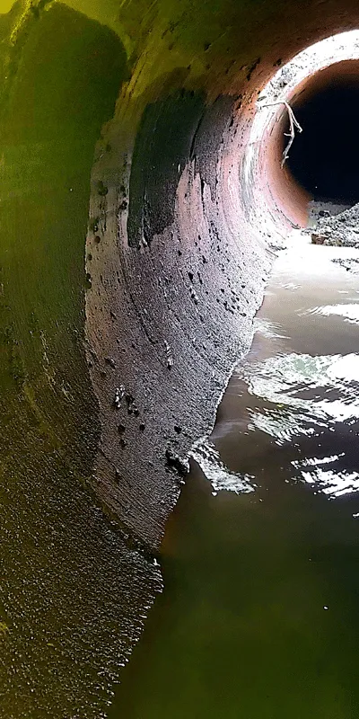 An interior view of a long dark pipe, with a portion lit up by light spilling in