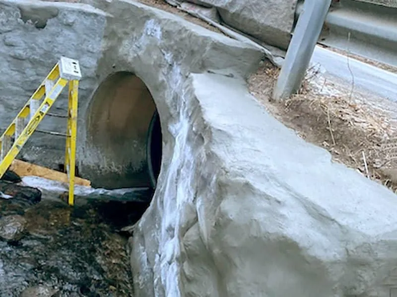 Concrete being applied to an aging headwall with technicians using ladders