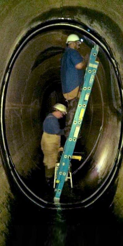 Two technicians installing HydraTite in an elliptical pipe