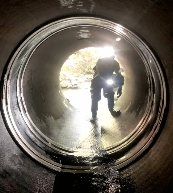 A technician pointing a flashlight at a HydraTite seal installed over a joint in a culvert