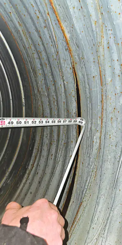A measuring tape being used while examining a compromised joint in a corrugated metal pipe