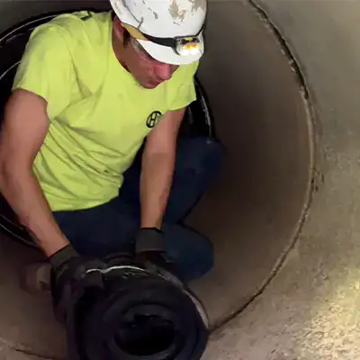 A technician positioning a rubber seal over a pipe joint inside a culvert