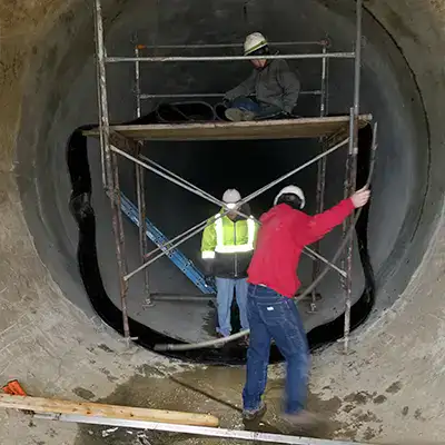 Several technicians installing HydraTite over a joint in a large-diameter pipe using scaffolding