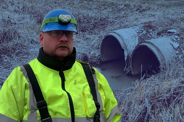 A technician standing in front of twin culverts running under a roadway