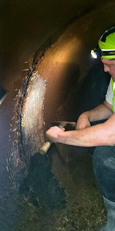 A technician using a hammer to remove tuberculation from the interior wall of a pipe