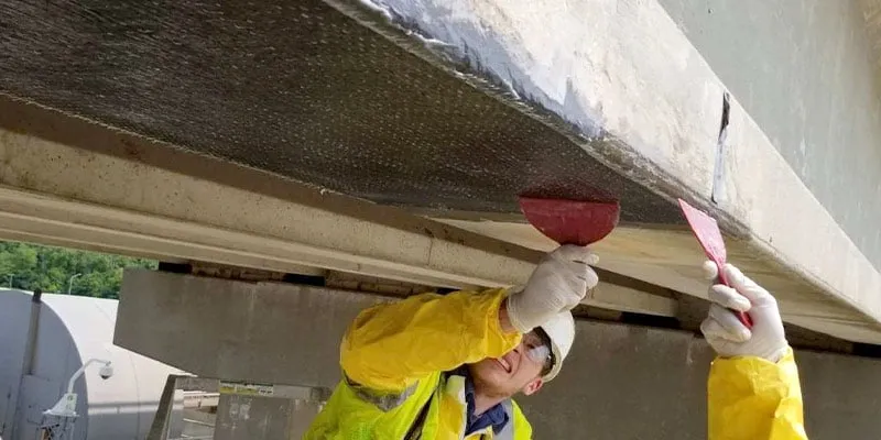 A technician applying epoxy to the underside of a bridge