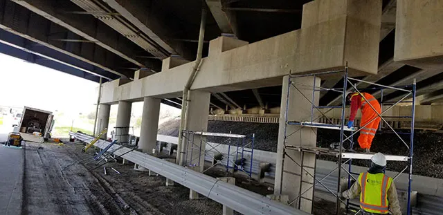 Technicians working on scaffolding to apply a carbon fiber composite to the bridge's pier caps