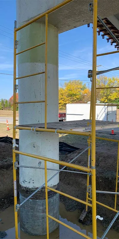 Scaffolding next a support column that is being wrapped in a composite resin and fiber fabric system