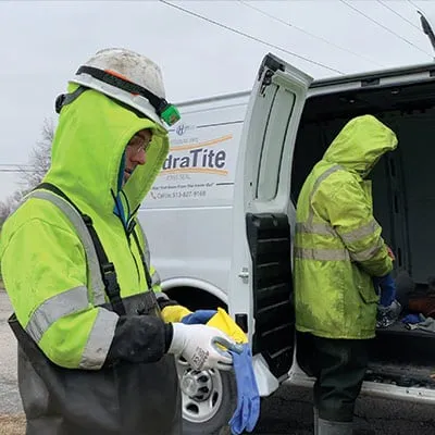 Two technicians preparing to enter a pipe to install HydraTite