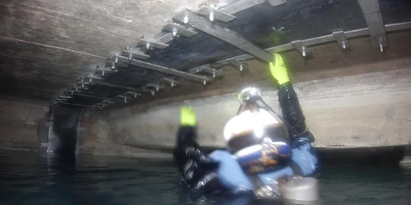 A diver partially out of the water installing HydraTite over a joint in a box-shaped culvert