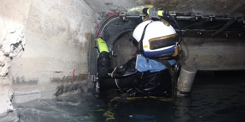 A diver partially out of the water installing HydraTite over a joint in a box-shaped culvert
