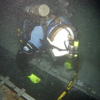 A diver kneeling in an underwater pipe installing HydraTite