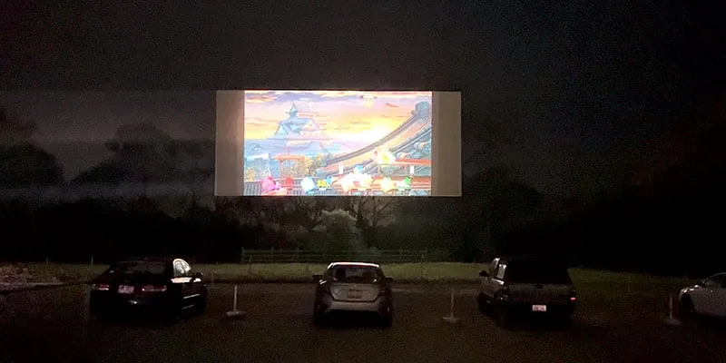 A drive-in screen with video games projected on to it with cars below