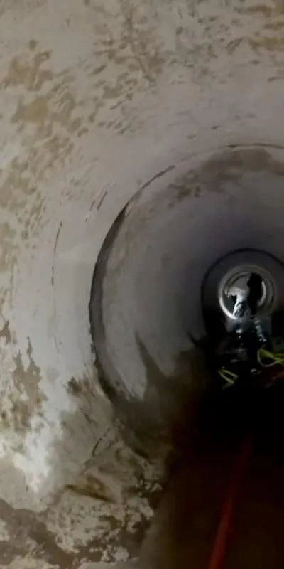 Looking down a dark pipe with a person deeper in the pipe with a light