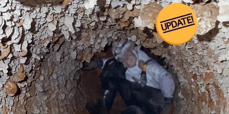 A person crouched in a pipe full of mineral build up all on the interior surface