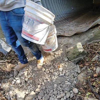 A person holding a bucket right outside a corrugate metal pipe