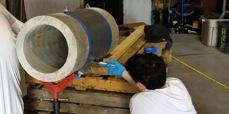 A person applying epoxy to the exterior of a small demo pipe