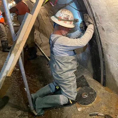 A technician kneeling inside a tunnel to install a HydraTite seal over three of the structure's sides