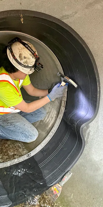 A technician with a hammer installing HydraTite over a joint in this concrete culvert