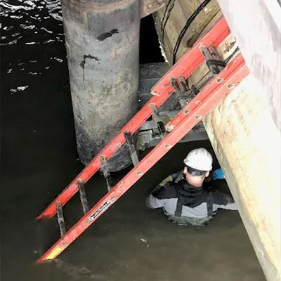 A technician standing in water working on a suspended outfall sanitary pipe