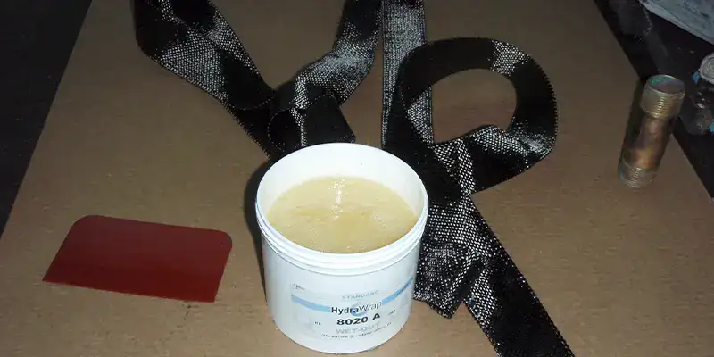An open tub of epoxy on a table next to a strip carbon fiber fabric