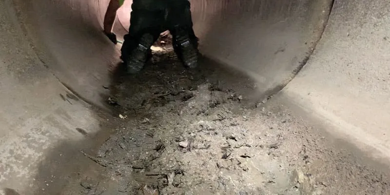 A inside view of a technician crawling through the inside of a dirty concrete pipe