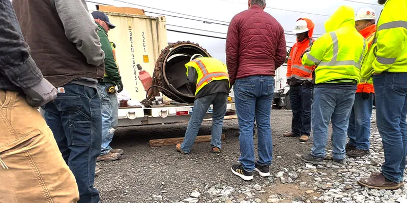 A person bent over, looking into a piece of pipe and explaining how HydraTite is installed