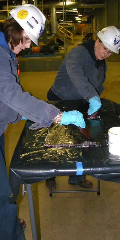 Technicians preparing carbon fiber fabric to be applied to the exterior of a cast iron pipe