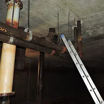 A ladder leaning against old pipe near the ceiling