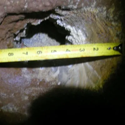 A measuring tape being used to determine the size of this wall defect in a pipe