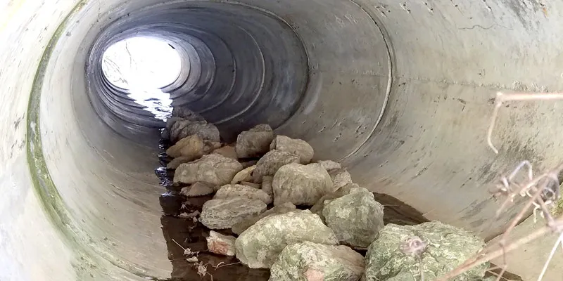 A concrete culvert with rocks scattered over the invert