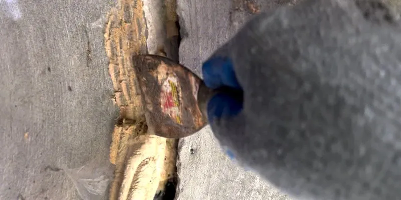 Scrapping away a bug's nest from the inside of a concrete culvert wall