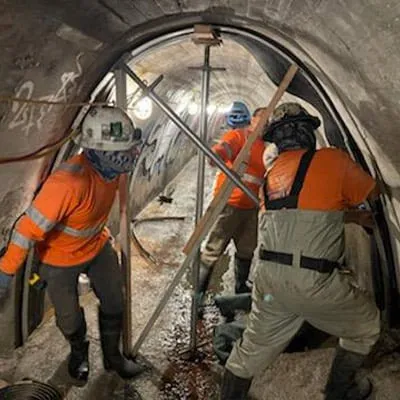 Three technicians installing HydraTite over a joint in an irregularly-shaped tunnel