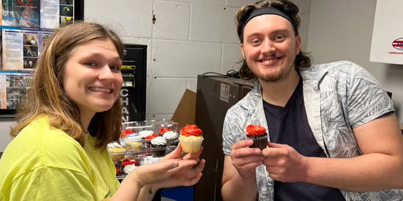 Two people holding up cupcakes and smiling