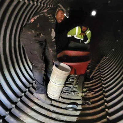 Two technicians working inside a corrugated metal pipe
